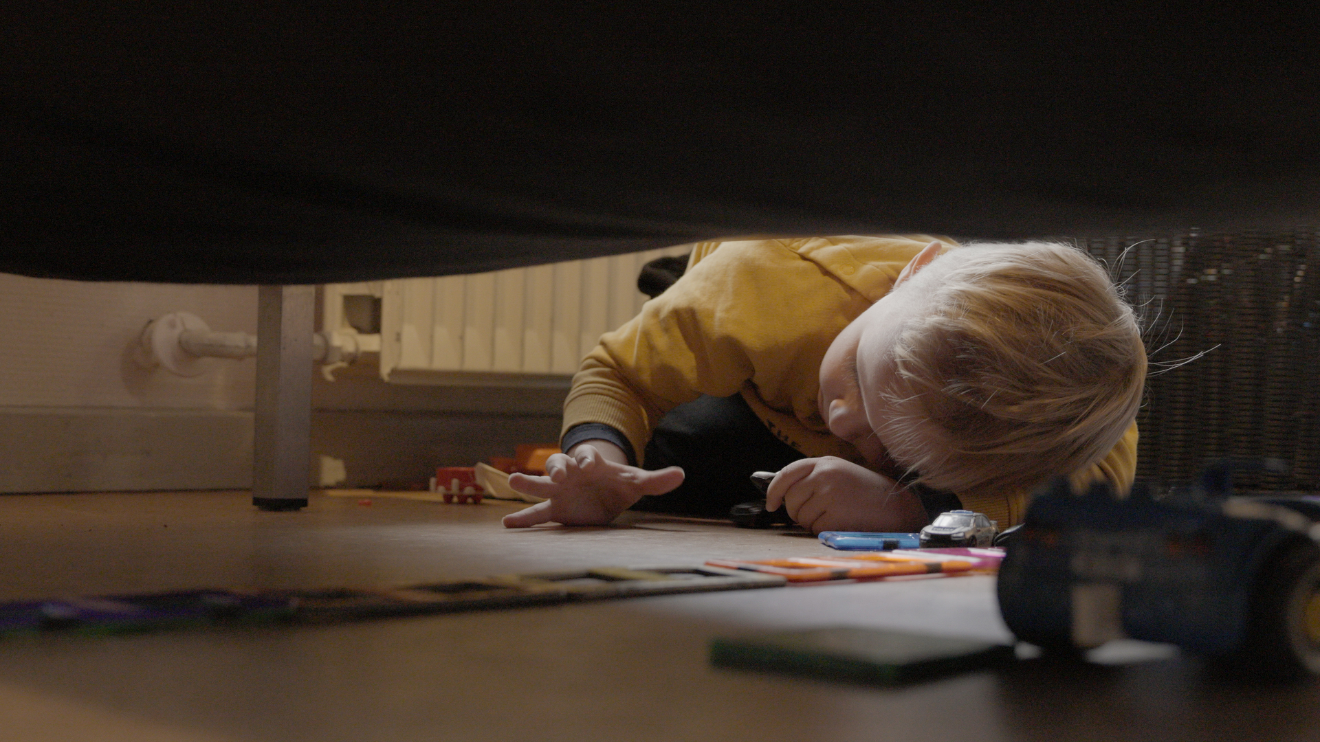 A child plays with toy cars under furniture in an indoor play area.