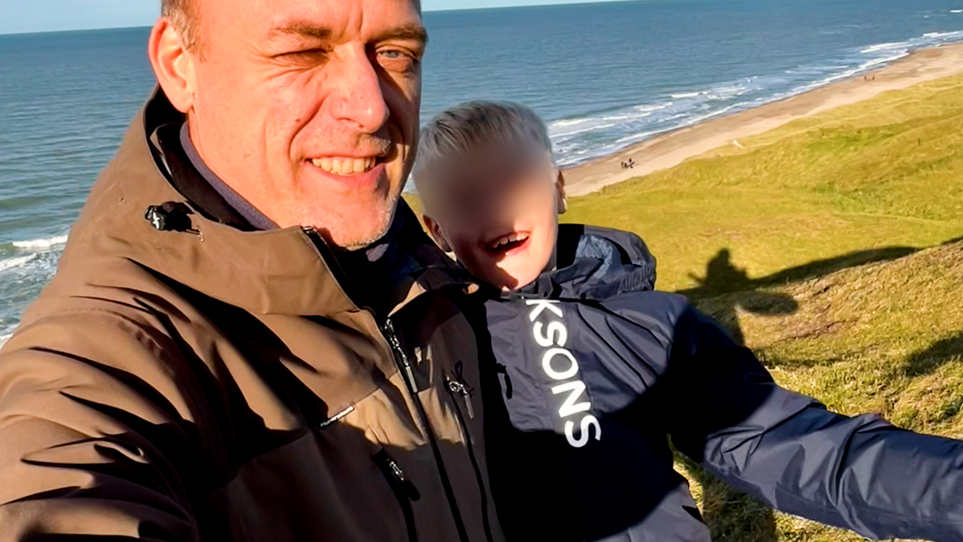 Father and son selfie with coast line in the background. Son's face blurred digitally.