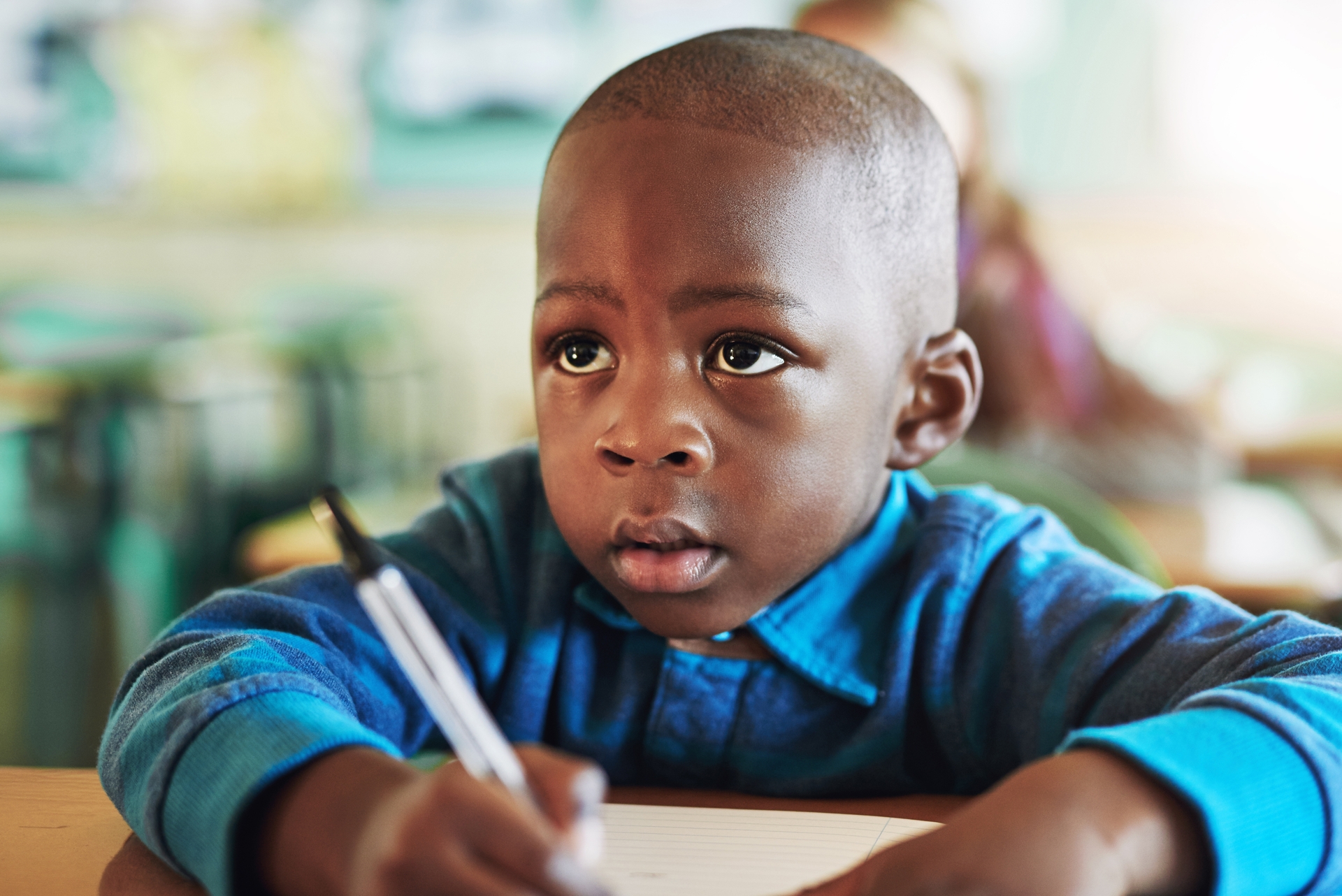 A child sits at a desk writing in a notebook with a pen.