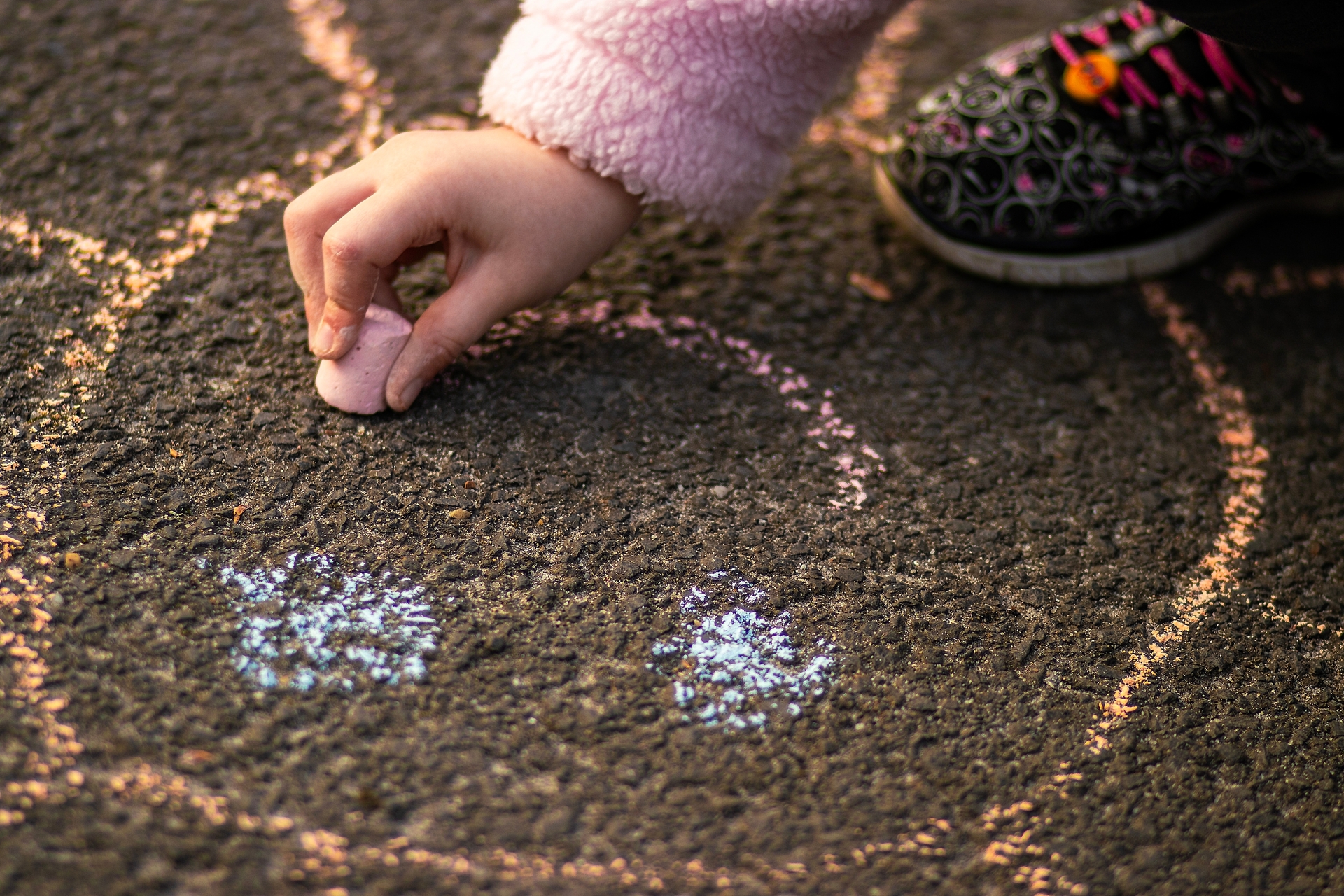 A child draws with pink chalk on asphalt.